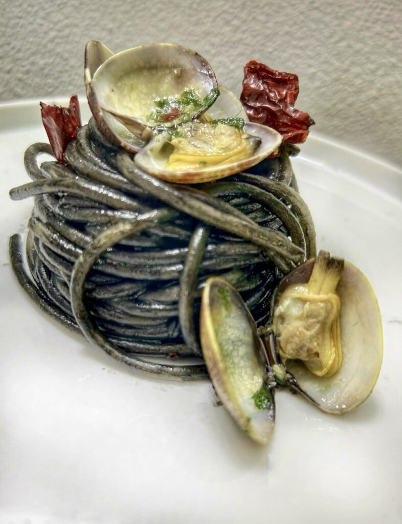 Spaghetti al nero di seppia, vongole veraci e chips di peperone crusco